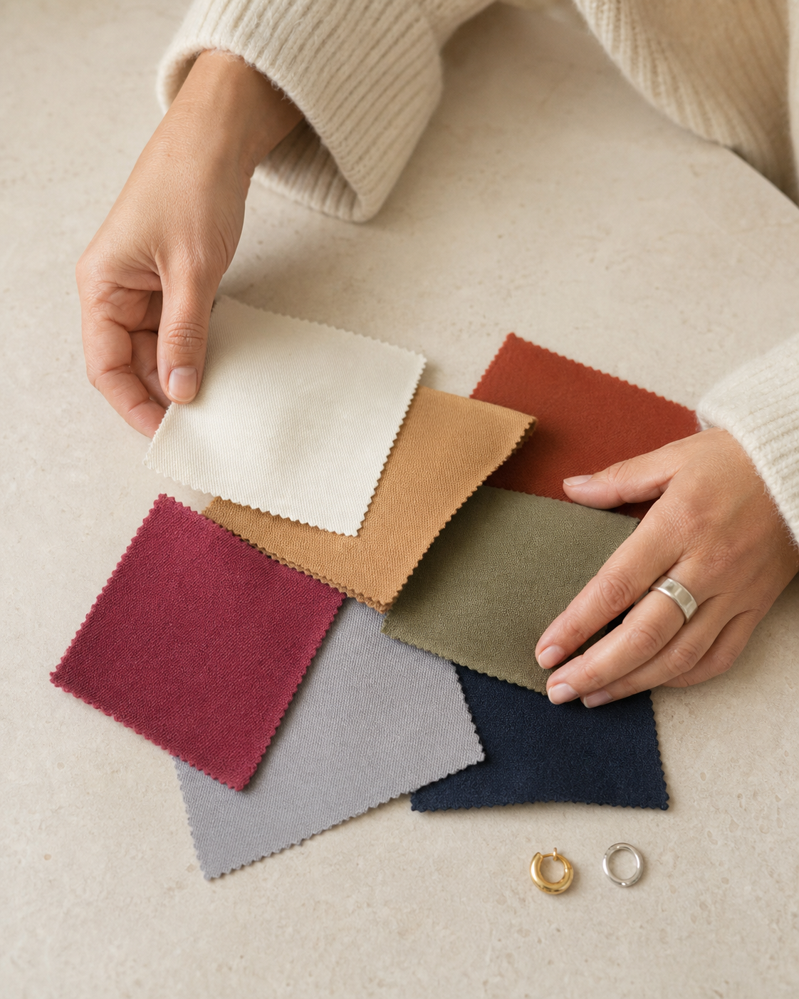 Hands comparing ivory, camel, rust, olive, navy, grey and berry fabric swatches