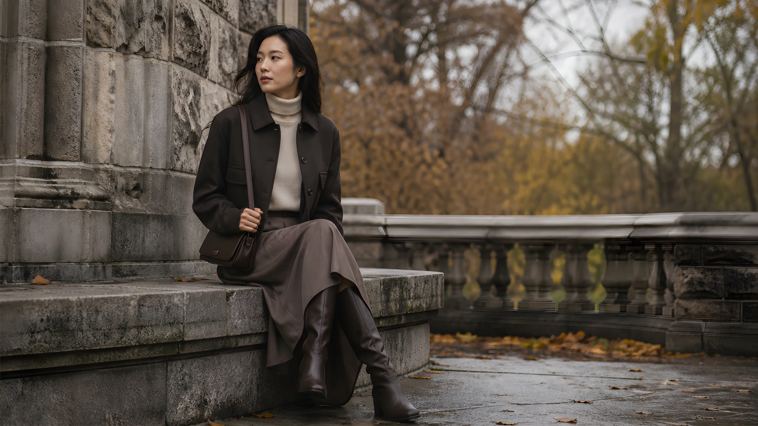 Asian model seated on stone steps in a dark jacket and soft neutral layers
