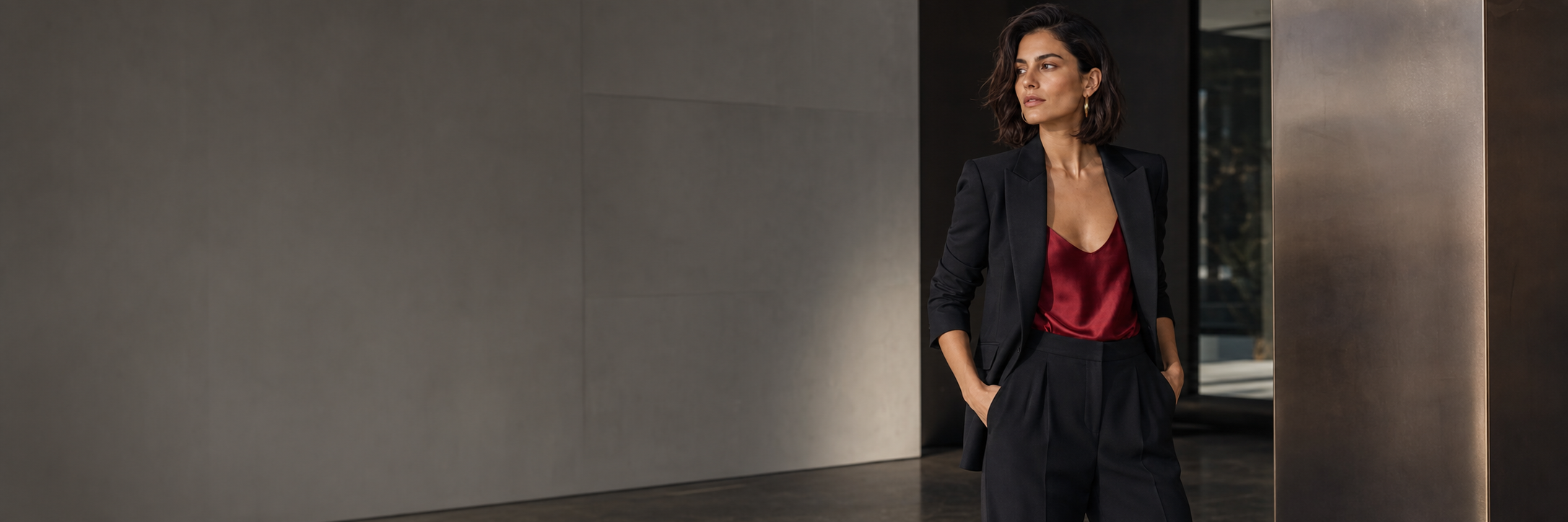 A woman in a tailored black suit with a deep-crimson satin top in a modern city interior